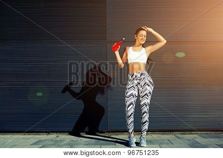Female runner hold energy drink bottle while resting after fitness training outdoors in the city