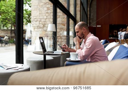 Young modern business man using smart phone and laptop computer in light loft interior