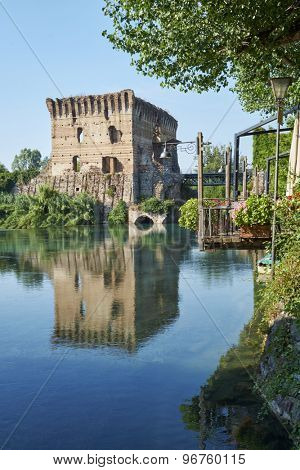 BORGHETTO, ITALY - JULY 11: Ruin of tower at Visconteo bridge, framed by vegetation and coasted by river Mincio. July 11, 2015 in Borghetto.