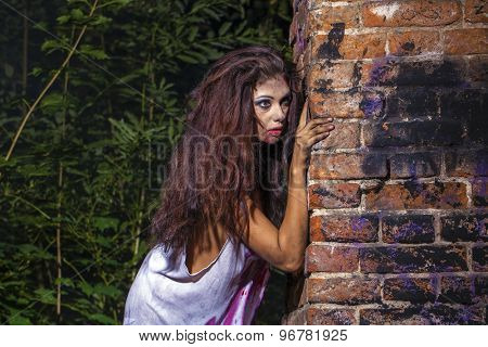 Sinister woman in a bloody shirt on dark brick wall