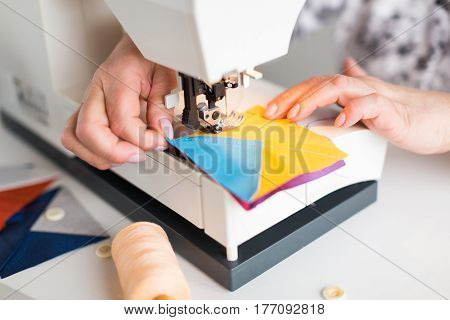 female hands scribbles on the sewing machine geometric color fabric pieces. the process of creating patchwork quilt. the fashion designer's hands at the sewing machine close up. hobby concept.
