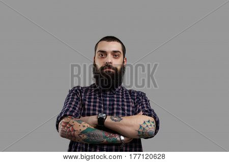 Isolated brutal bearded man with tattooed hands on grey background. Football fun look to the camera. Guy drink a lof of beer and have big stomach. Serious emotion on the face of aggressive person.