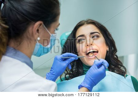 Young woman at the dentist. Stomatologist holding concave mirror. Check your teeth.