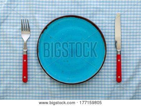 Empty blue ceramic plate with knife and fork close up top view