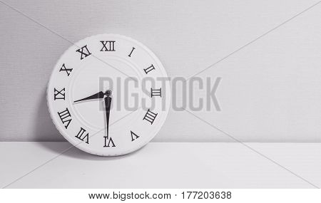 Closeup white clock for decorate show half past eight o'clock or 8:30 a.m. on white wood desk and wallpaper textured background in black and white tone with copy space