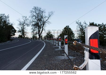 Road fence barrier. Canyon road with prominent tree and nice evening sky. Traffic Barrier safety road on road. Close up asphalt road texture with white stripe