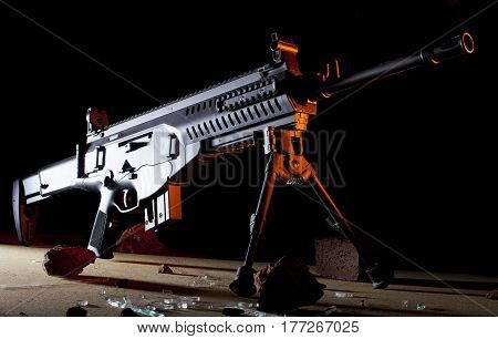 Semi automatic black rifle with orange light from the side on a dark background