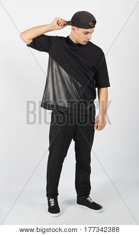 Young muscular man wearing black clothes and sneakers isolated on white background. He is holding snapback and looking down.