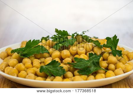 Parsley and chickpeas. Plate of cooked cheak peas and leaves of fresh parsley on a plate on wooden table background