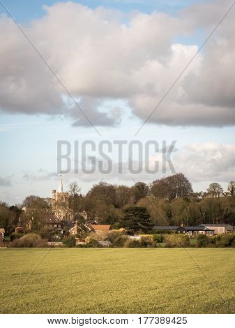 A view of the rural English village of Ivinghoe in the heart of Buckinghamshire in the South of England set against a fallow crop field and dramatic winter sky on a sunny day.