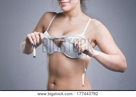 Woman in white underwear measuring breast volume on gray background perfect female body
