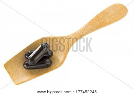 Top view of 3 dark black medicine soft gel capsules on wooden spoon isolated on white background