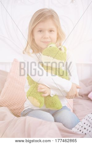 Little girl sitting on a bed and hugging her frog mascot