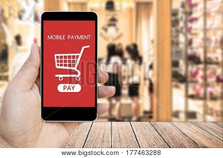 Hand holding smart phone with mobile payment and Shopping Cart on screen over blur people in the shopping mall background business and financial concept.