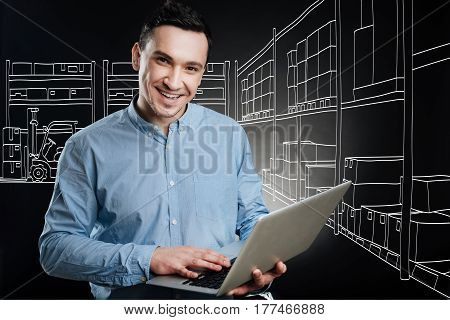 Plan all the work. Professional positive logist working in a depository and using laptop while sharing positivity