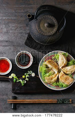 Gyozas potstickers on lettuce salad with sauces. Served in traditional china plate with chopsticks and black teapot on wood serving board over old metal background. Top view, space. Asian dinner