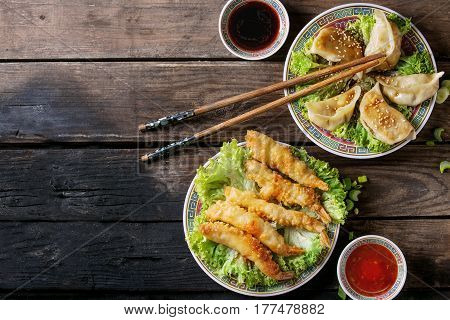 Fried tempura shrimps and gyozas potstickers on lettuce salad with sauces and rice. Served in traditional china plate with chopsticks over old wooden background. Top view. Asian dinner