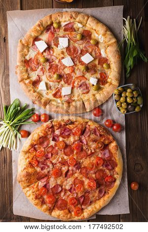 Rustic pizza with salami mozzarellabasil top view with copy space. Two pizzas on a wooden table. Pizza salami on wooden background. Pizza salami with tomatoes and olives