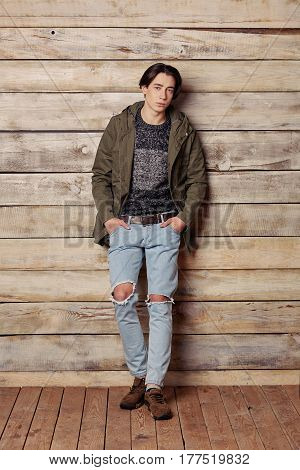 Handsome man wearing green jaket and torn jeans in wooden rural house interior