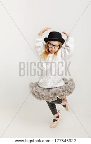 Cute little girl hipster ballerina in a ballet tutu pointes glasses and a hat. The younger generation of dancers.