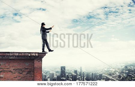 Businessman with blindfolder on eyes walking on building top