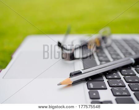 Laptop, notebook,gresses and pencil on the green grass