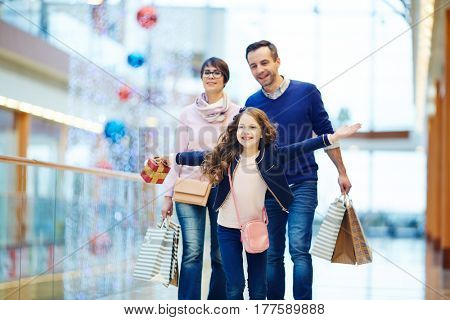 Girl with gift box running in front of her parents during shopping