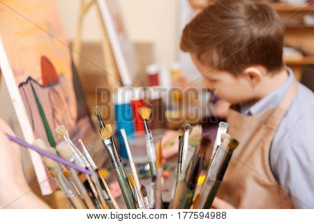 Involved in my thoughts. Involved hardworking pleasant boy sitting in the workshop and having art class while showing his abilities and painting