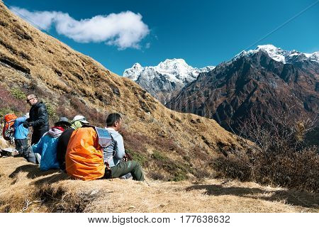 Group of Hikers with Backpacks resting on rocky Footpath observing Mountain Panorama with high Peaks on Background