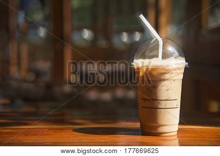Cold coffee in plastic cup on brown wooden table at cafe.