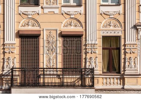 Windows with grilles moldings and a balcony with a metal grating on the facade of the beige building. From the window series Saint-Petersburg.