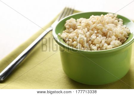 Green ceramic bowl full of brown rice on napkin