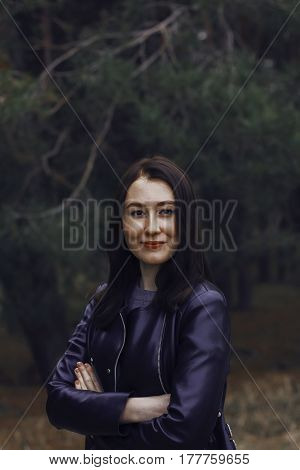 Girl with dark hair in the forest. She wears a black leather jacket. Portrait of a smiling girl with freckles.