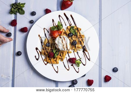 Plate of belgian waffles with ice cream chocolate sauce and fresh berries