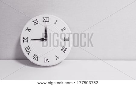 Closeup white clock for decorate in 9 o'clock on white wood desk and wallpaper textured background in black and white tone with copy space