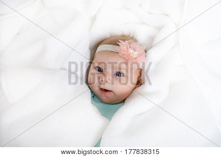 Cute adorable newborn baby in white bed and wrapped in blanket. New born child, little girl looking surprised at the camera. Family, new life, childhood, beginning concept.