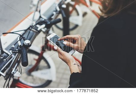 Young businesswomen in black suit and umbrella using smartphone biking and going to work by city bicycle on urban street hipster girl holding mobile gadget ecology environment concept