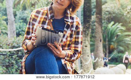 Hipster person holding in hands digital tablet with screen young girl smile reading on computer on background nature park palm landscape flare mock up technology blur female hands tourist using gadget