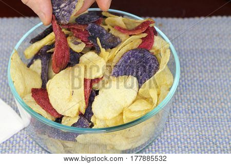 Adult male fingers picking up one of each of three colors of potato chips. Yellow red and purple potato chips chosen by fingers of an adult male.