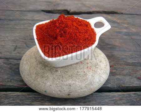 Red chilli powder filled bowl on rounded stone