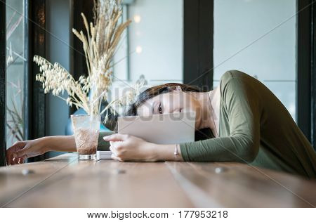 Closeup asian woman lied on the wooden counter desk for reading a book in coffee shop with happy face on blurred coffee shop view background under window light