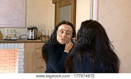 Beautiful brunette woman with long black silky hair puts on and wears earrings and smartens up in front of mirror in make-up dressing room.