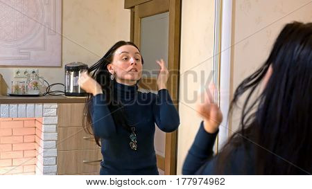 Beautiful brunette woman drying long black silky hair and smartens up in front of mirror in make-up dressing room.