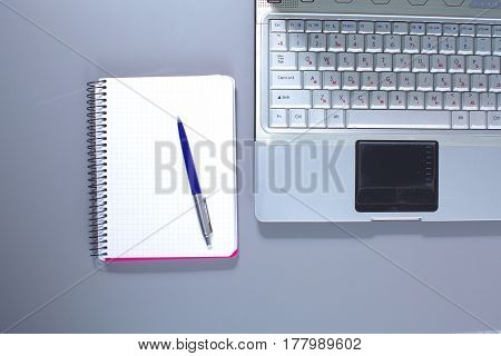 A note book, laptop, pen, graph paper document on the office desk table behind white blind.