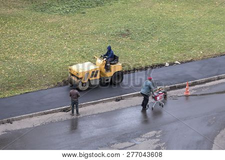 Road Construction Worker Compactes Fresh Asphalt With Roller Compactor Machine. Another Worker Overw