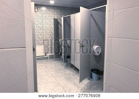 The Interior Of A Public Toilet With Open Doors Stalls In Gray Tones. Artificial Lighting, Gray Tile