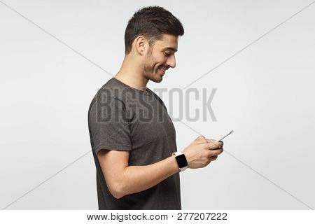Side Portrait Of Handsome Man, Wearing Smart Watch, Isolated On Gray Background, Looking At Smartpho
