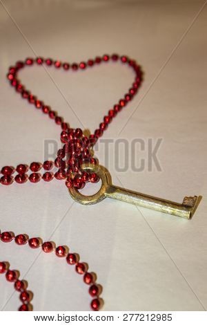 Old Shabby Key Tied With Red Heart-shaped Beads And Lying On White Background Close-up