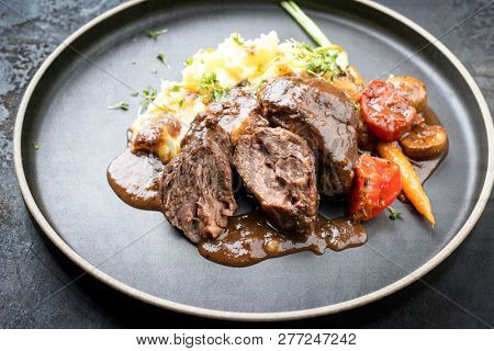 Traditional German braised pork cheeks in brown sauce with mushroom and mashed potatoes as closeup on a modern design plate