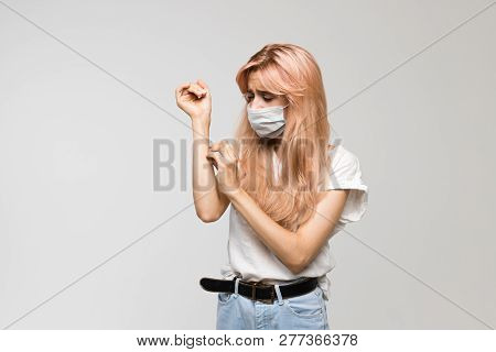 Isolated studio portrait of young beautiful woman with medical mask in white t-shirt scratch itch hand, irritation, sensitive skin, allergy symptoms, rhinitis, cold/healthcare and medicine concept.